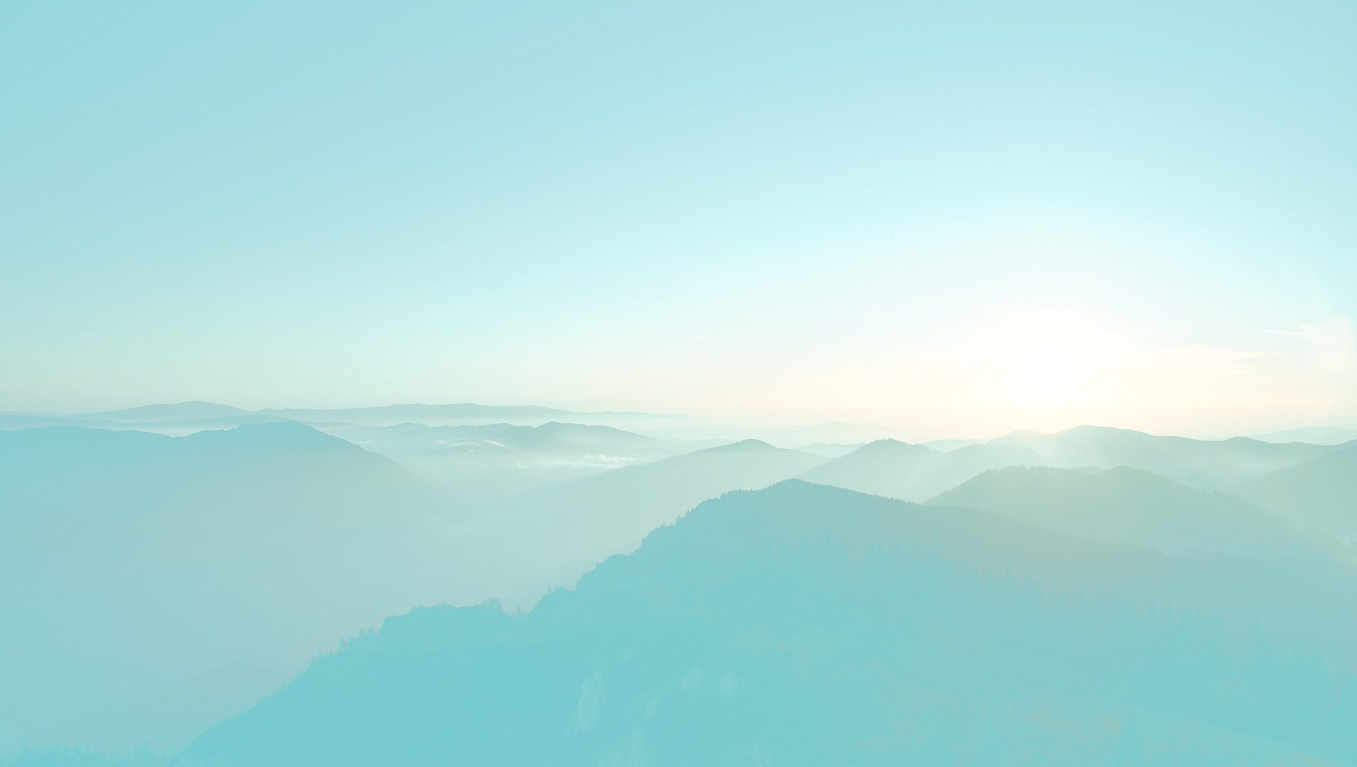 Weite Berglandschaft im Morgennebel unter hellblauem Himmel